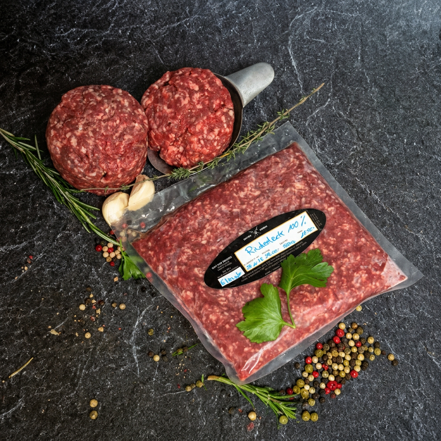 Rinder-Hack vom Weiderind, vakuumverpackt und als zwei offene Portionen, mit Kräutern, Knoblauch und Pfefferkörnern auf dunklem Steinuntergrund.