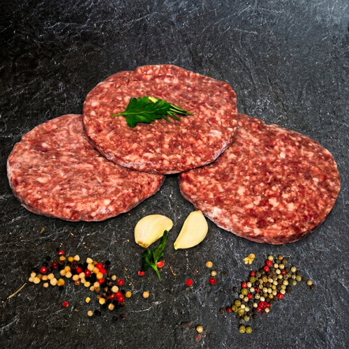 Drei Rindfleisch-Burger-Patties (Beef-Burger) von Gut-Hof-Gruber auf dunkler Steinplatte mit Petersilie, Knoblauch und Pfefferkörnern.