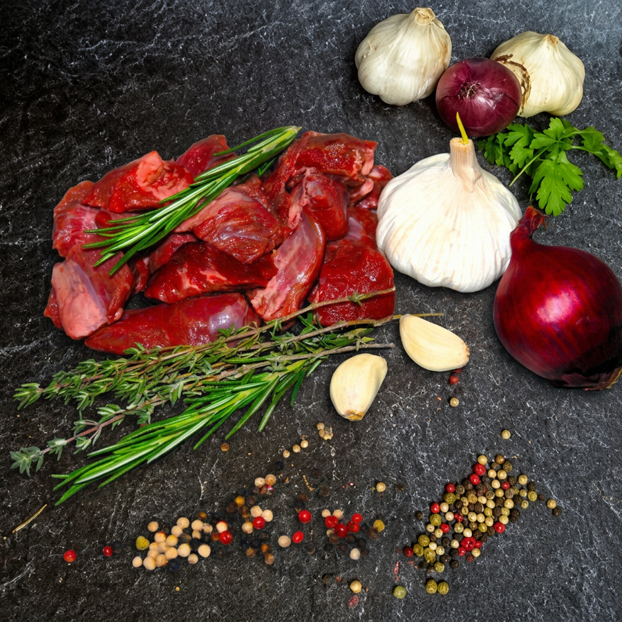 Rindergulasch in rohen Fleischstücken mit Rosmarin, Thymian, Knoblauch, roter Zwiebel und Pfefferkörnern auf Steinuntergrund.